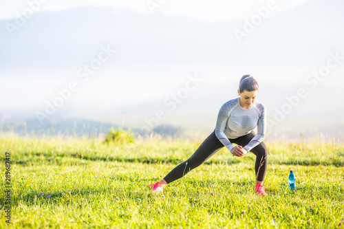 Young fitness woman runner stretching legs before run in autumn nature