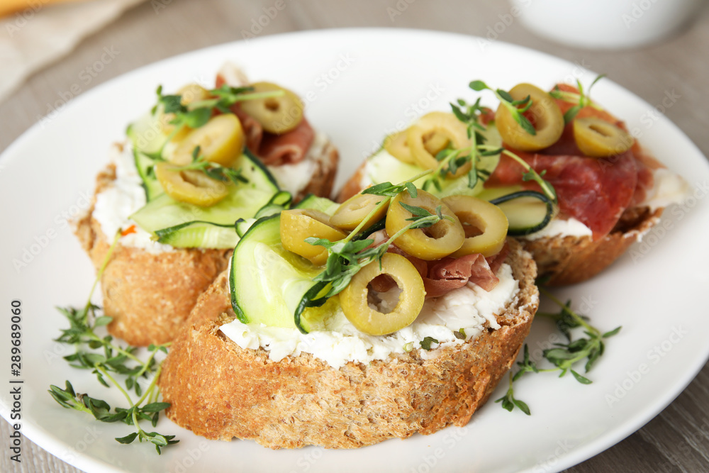 Plate of delicious bruschettas with prosciutto on table, closeup