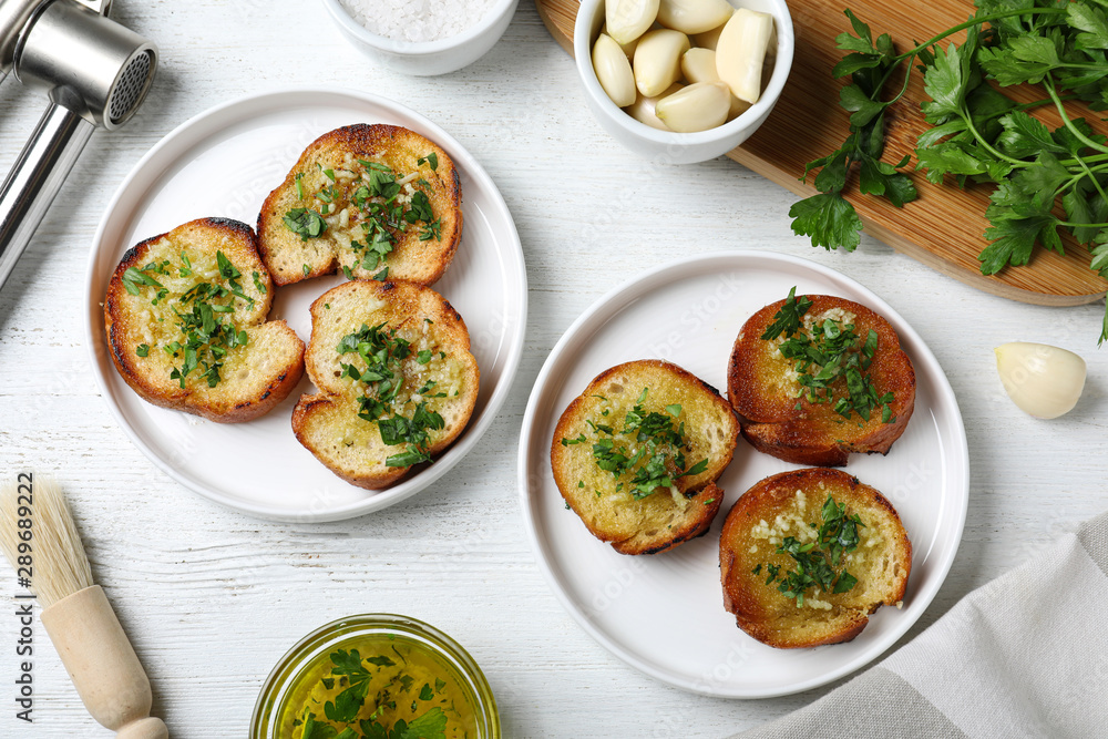 Slices of toasted bread with garlic and herb on white wooden table, flat lay Slices of toasted bread with garlic and herb on white wooden table, flat lay