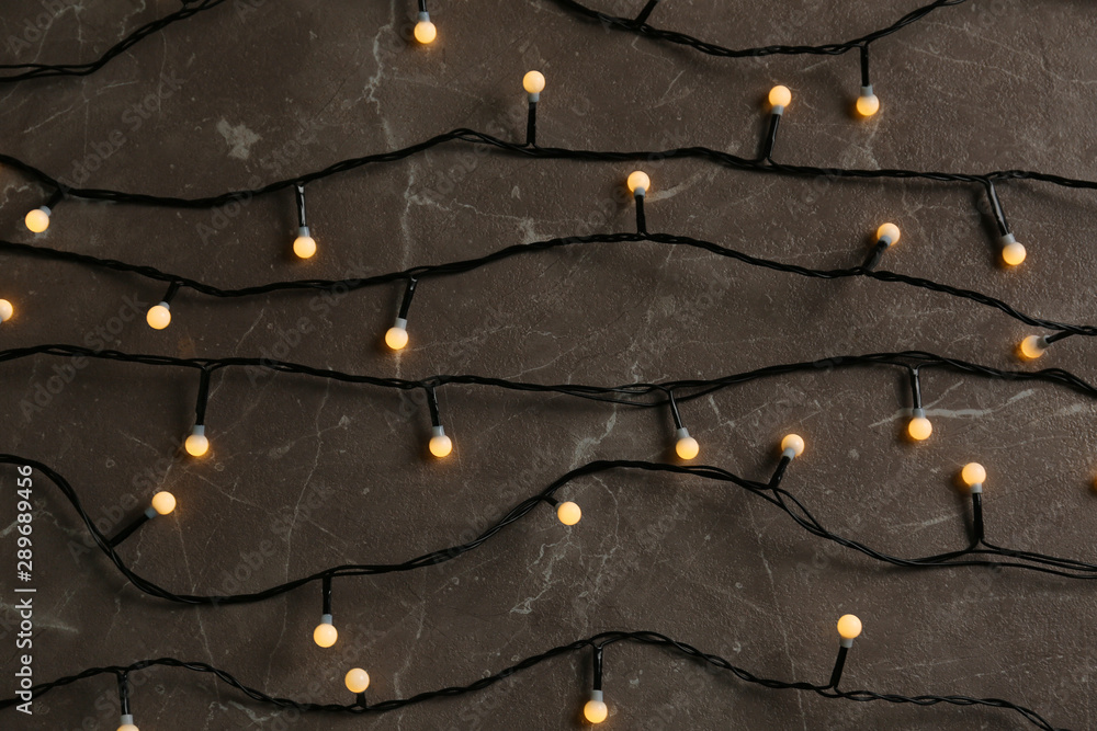 Glowing Christmas lights on grey marble background, top view