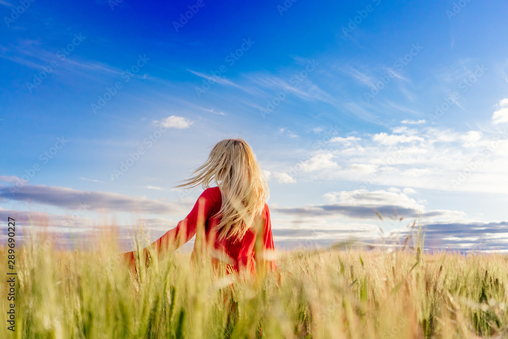 Obraz premium Blonde girl in a field with developing hair in a red dress