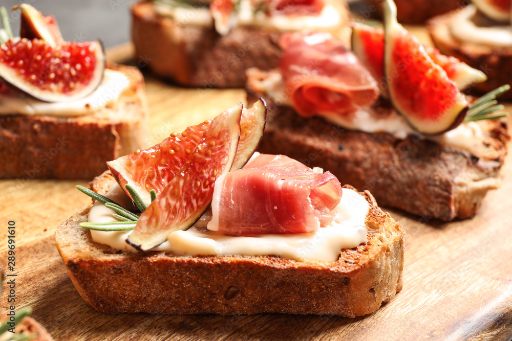 Bruschettas with cream cheese, prosciutto and figs served on wooden board, closeup Bruschettas with cream cheese, prosciutto and figs served on wooden board, closeup