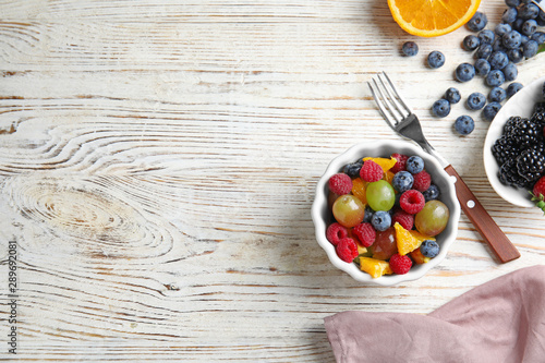 Fresh tasty fruit salad on white wooden table, flat lay. Space for text