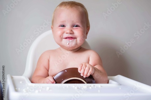 A young child sits in a highchair and eats cottage cheese. Finger food for the development of fine motor skills. Smiling little girl.
