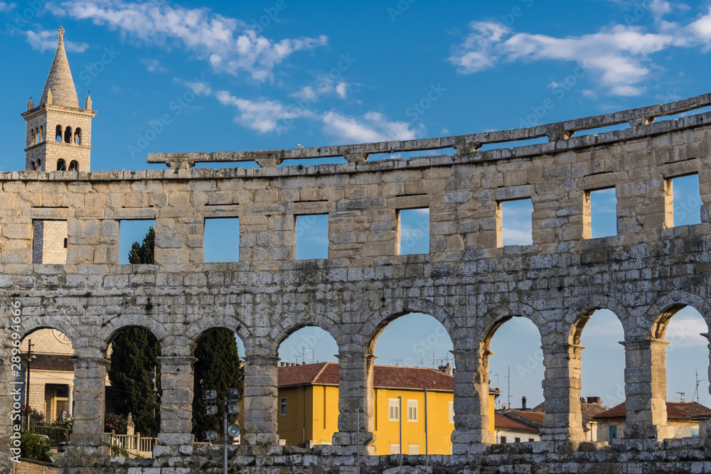 Arched walls of Pula Arena (Arena di Pola) with the Pula city view, Roman amphitheatre with the blue sky on background in Pula, Croatia - Image
