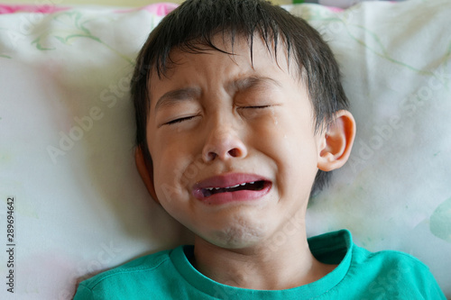 The lovely Asian boy in the green t-shirt is sad and crying on the bed at home.Unhappy and tired expression kid concept. photo