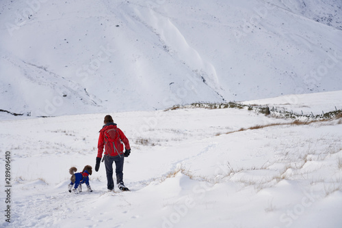 A hiker and their dog walking through fresh snow while descending from The Knott towards Hayeswater Gill near Hartsop in the Lake District.