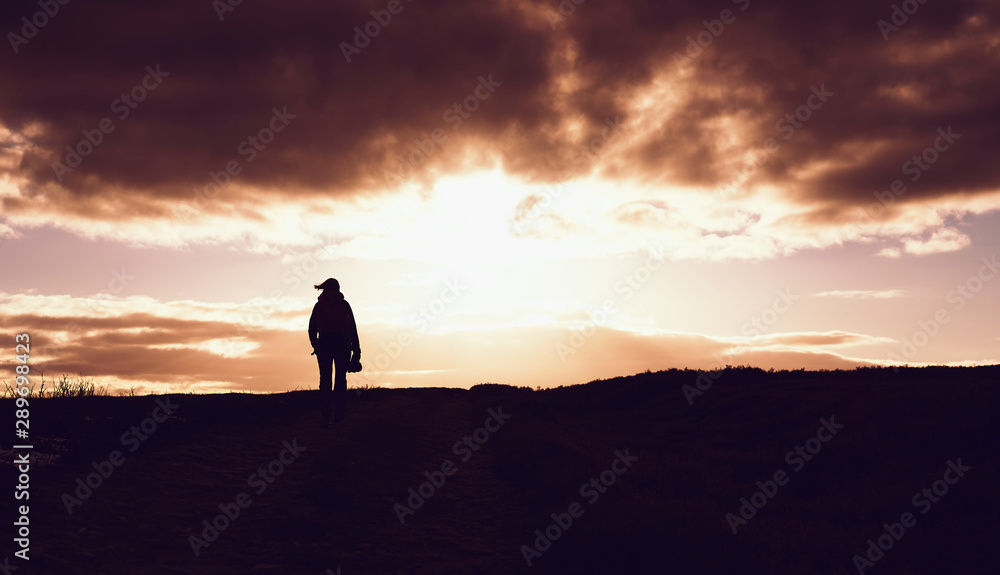 The silhouette of a hiker on the left of the frame against a fire red sky at sunset over the open moors.