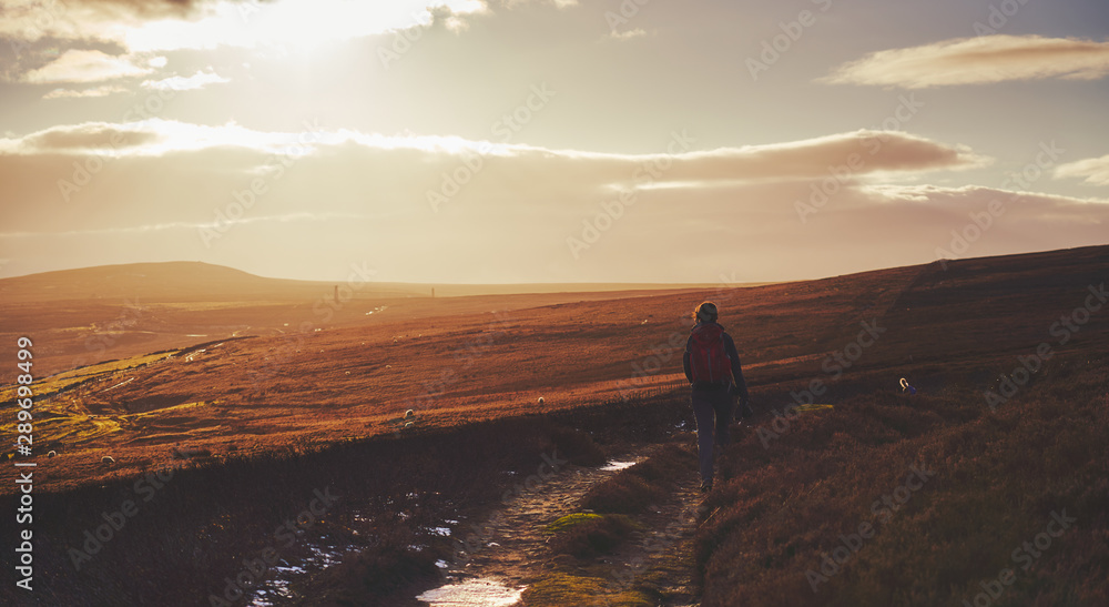 A hiker walking along a winding path at sunset towards the old stone chimney's at Bolts Law in County Durham