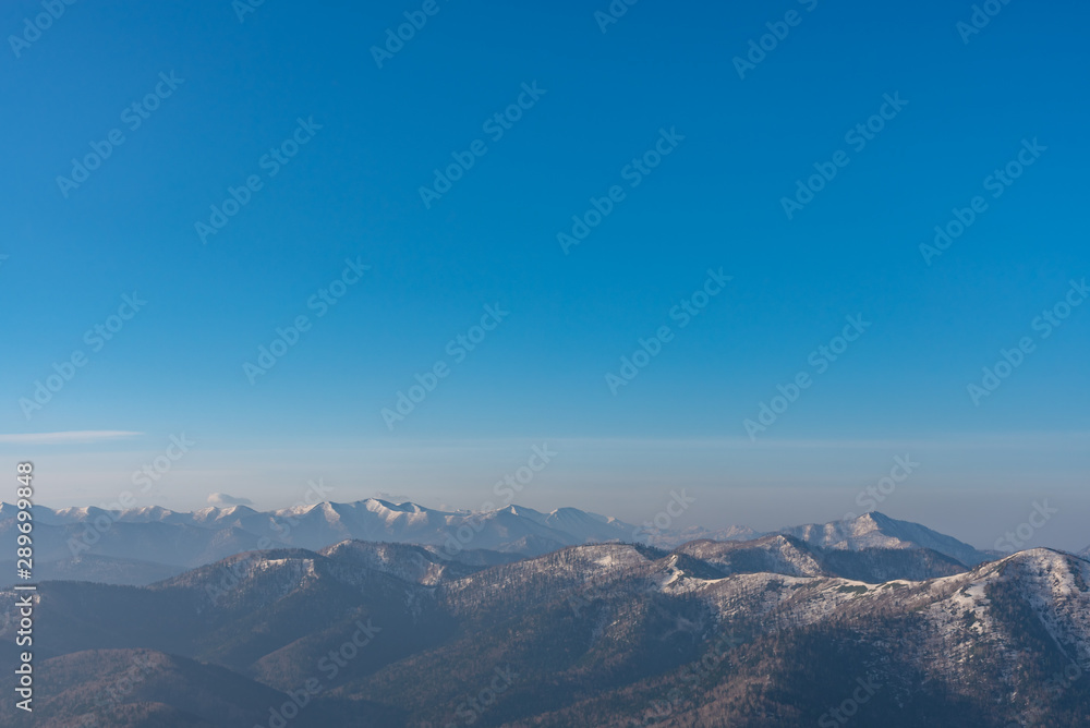 Fototapeta premium Panoramic view of beautiful mountain landscape, snowy mountain peaks covered by forest with a dark blue clear sky background in spring time sunny day