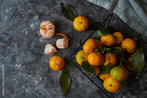 Juicy tangerines with leaves in a basket on a dark background