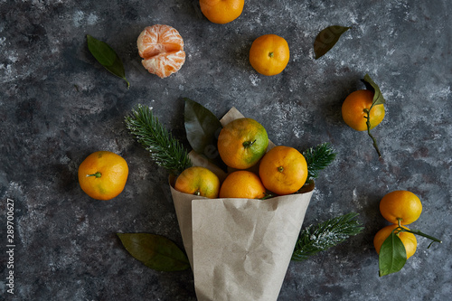 Juicy tangerines with leaves and fir branches in a paper bag on a dark background