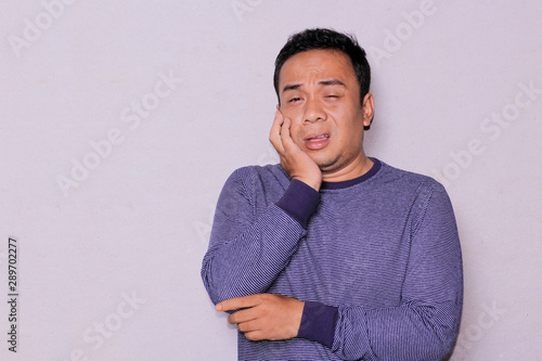 an asian man tooth ache expression while holding his cheeck. photo