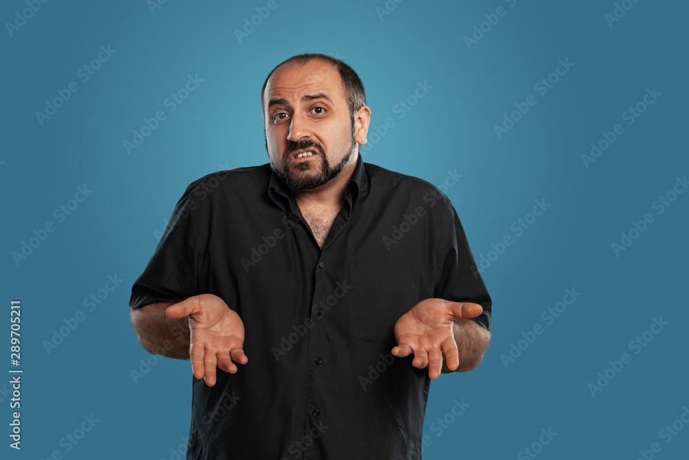 Close-up portrait of a brunet middle-aged man with beard, dressed in a black t-shirt and posing against a blue background. Close-up portrait of a brunet middle-aged man with beard, dressed in a black t-shirt and posing against a blue background.