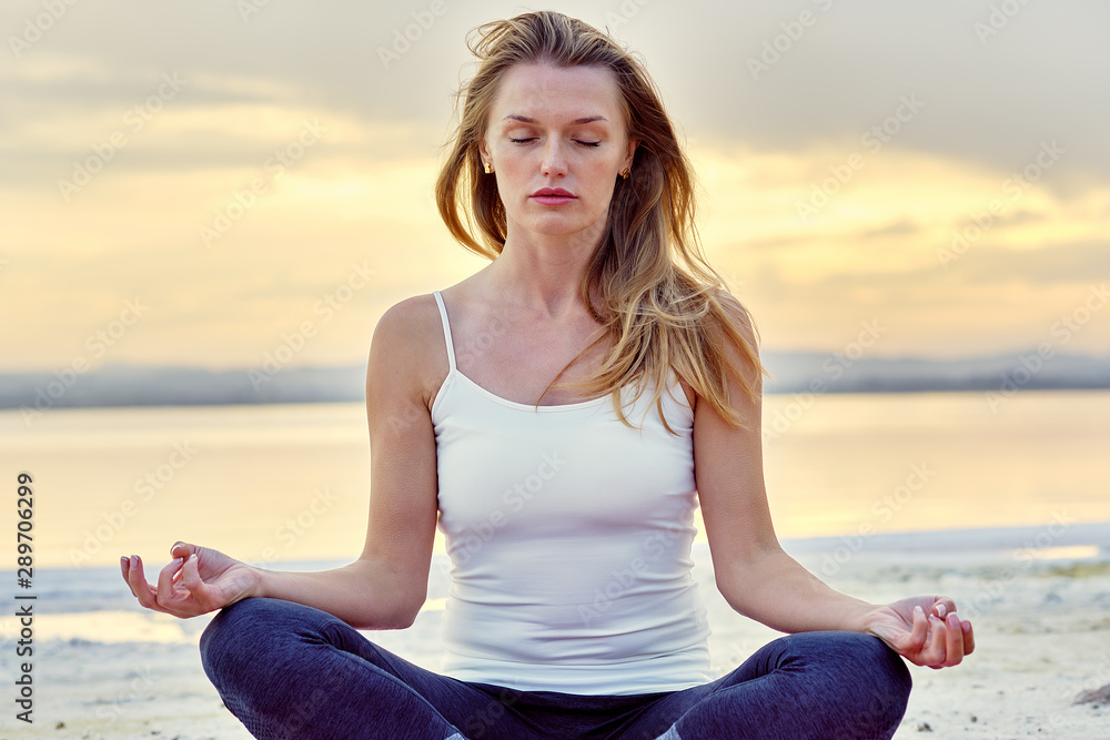 Alone yogi woman seated in lotus position meditating near lake