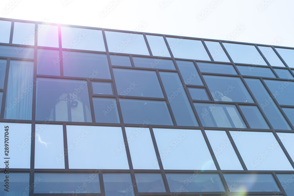 Fototapeta premium Minimalism in street photography. Glass office building against the blue sky. Modern design and straight lines - urban texture.