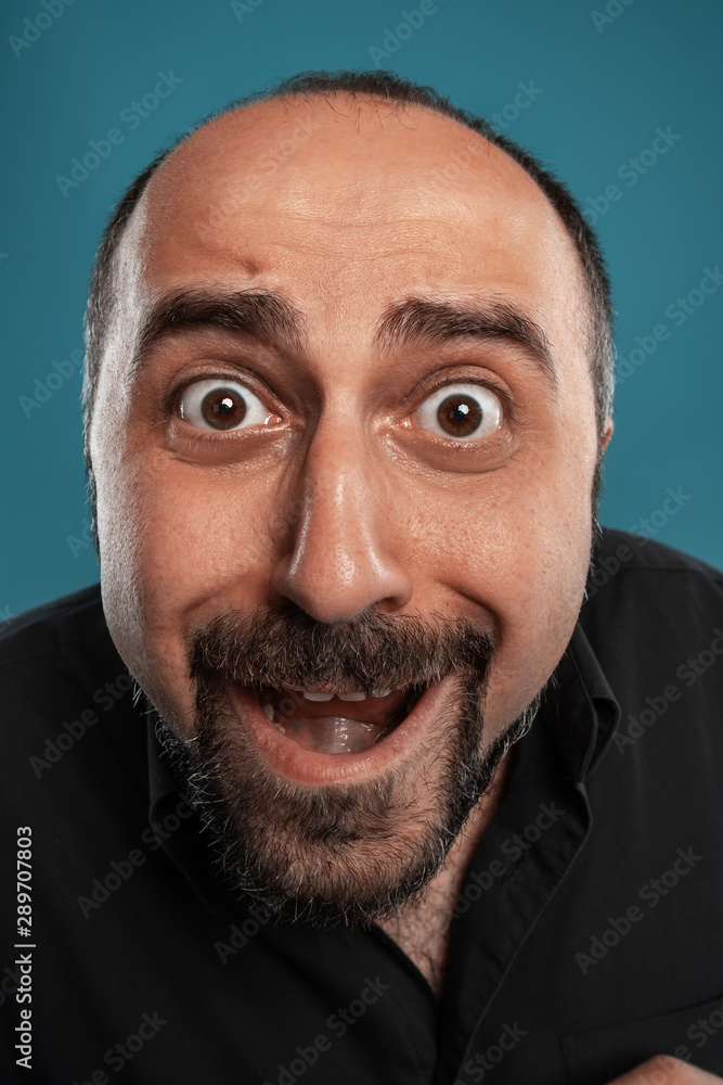 Close-up portrait of a brunet middle-aged man with beard, dressed in a black t-shirt and posing against a blue background. Close-up portrait of a brunet middle-aged man with beard, dressed in a black t-shirt and posing against a blue background.