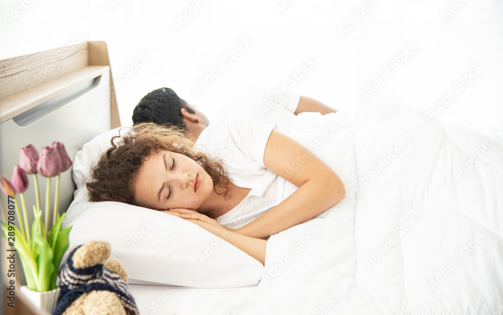 Unhappy young couple lying and sleeping under white blanket in bed Caucasian beautiful woman and Asian handsome man sleeping on bed back to back. Unhappy young couple lying and sleeping under white blanket in bed Caucasian beautiful woman and Asian handsome man sleeping on bed back to back.