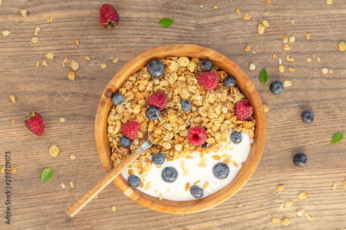 Yogurt with granola and berries fresh raspberries and blueberries on wooden background. Top view. Delicious and healthy Breakfast smoothie. Vegetarian food.