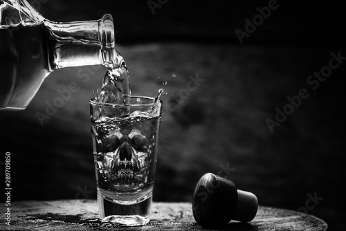 Drink bottle and glass with alcohol content. Image of translucent skull in glass. Alcoholism, addiction or poison concept.
