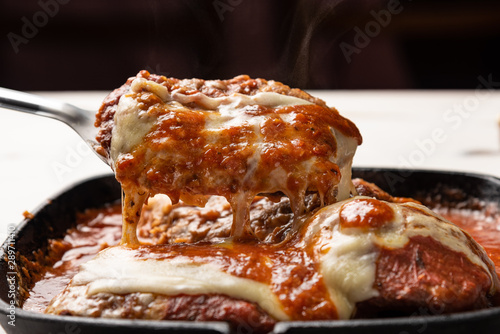 Parmegiana Steak also known as Filet Parmegiana in a black iron pan on a wooden white background, cheese and tomato sauce. Soft light, angle view