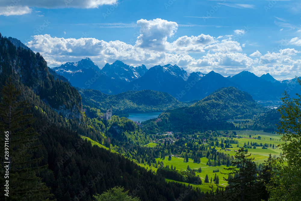 Bergflanke mit frischem Grün im Vordergrund, blauer See und Bergmassiv im Hintergrund