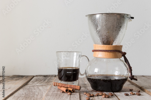 Homemade drip coffee using glass jug and metal filter with beans on wooden table over white background