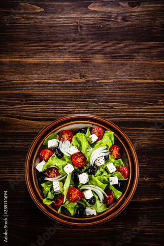 Greek salad in bowl on wooden table