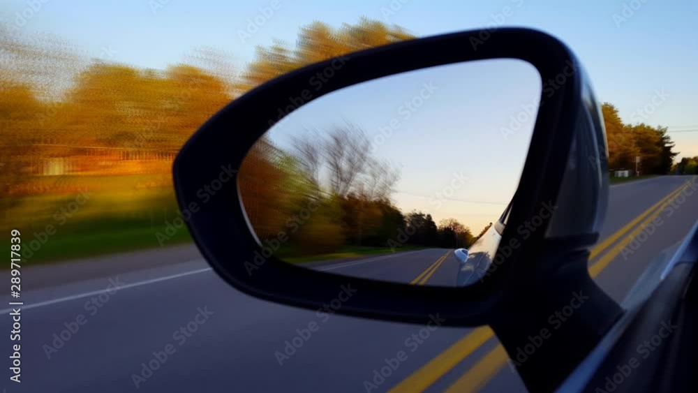 *Motion Blur Version* Driving Rural Road View of Side Mirror at Sunset. Driver Point of View POV Looking Down Side View Mirror Near Dusk Along Beautiful Country Street. *Motion Blur Version* Driving Rural Road View of Side Mirror at Sunset. Driver Point of View POV Looking Down Side View Mirror Near Dusk Along Beautiful Country Street.