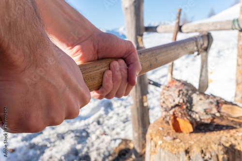 Hands of a man chopping wood with an axe.