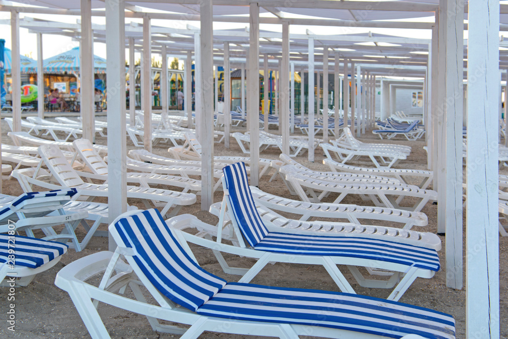 Lots of beach plastic white sun loungers. Several chaise lounges in mattress covers, in a white and blue strip. Awning - a white wooden structure covered with a white cloth. Summer vacation at sea. Lots of beach plastic white sun loungers. Several chaise lounges in mattress covers, in a white and blue strip. Awning - a white wooden structure covered with a white cloth. Summer vacation at sea.
