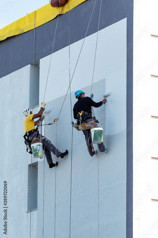Fototapeta premium pintores colgados de un arnés pintando una fachada