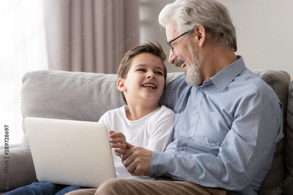Happy old grandfather and grandson laughing using laptop on sofa Happy old grandfather and grandson laughing using laptop on sofa
