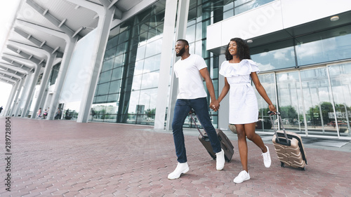 Happy african american couple running with luggage at airport exterior
