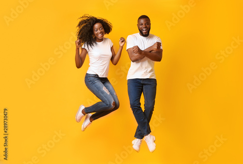 Funny african couple jumping in the air over yellow background