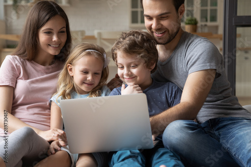 Happy young parents sitting with cute little kids, using computer.