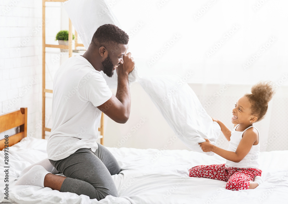 Fototapeta premium African father and little daughter having pillow fight on bed
