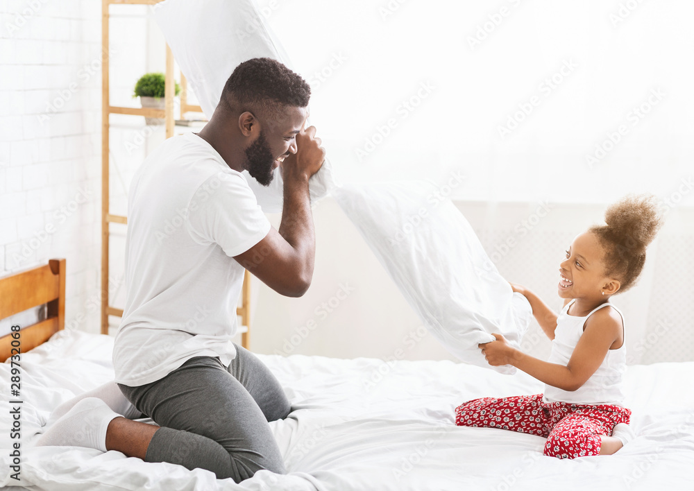 African father and little daughter having pillow fight on bed