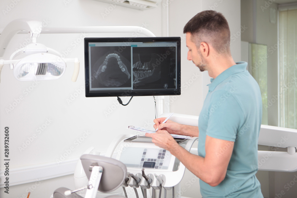 A male dentist looks at a screen shot of a jaw. A snapshot on the monitor screen. The figure of the doctor is out of focus. Concept of conservation and treatment of teeth. A male dentist looks at a screen shot of a jaw. A snapshot on the monitor screen. The figure of the doctor is out of focus. Concept of conservation and treatment of teeth.