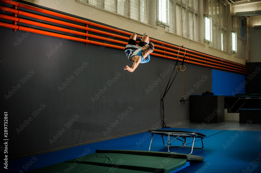 Naklejka premium Man jumping from the trampoline to the mat in the gym
