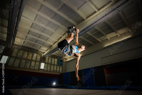 Young man making tricks on the trampoline in the gym