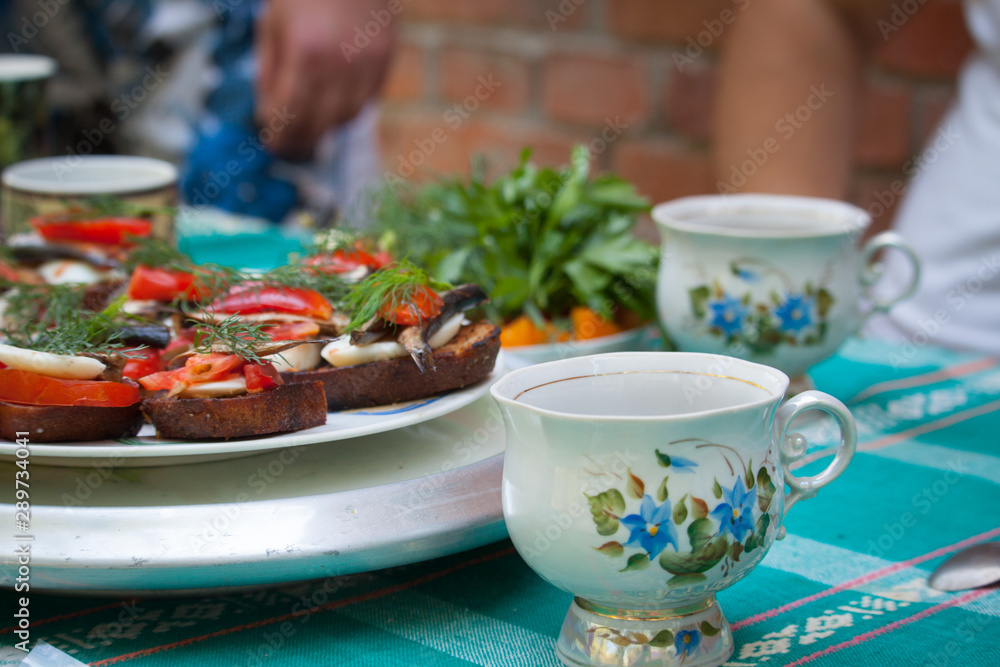 Outdoor picnic, sandwiches with egg, tomato, sprats and teacups, selective focus Outdoor picnic, sandwiches with egg, tomato, sprats and teacups, selective focus