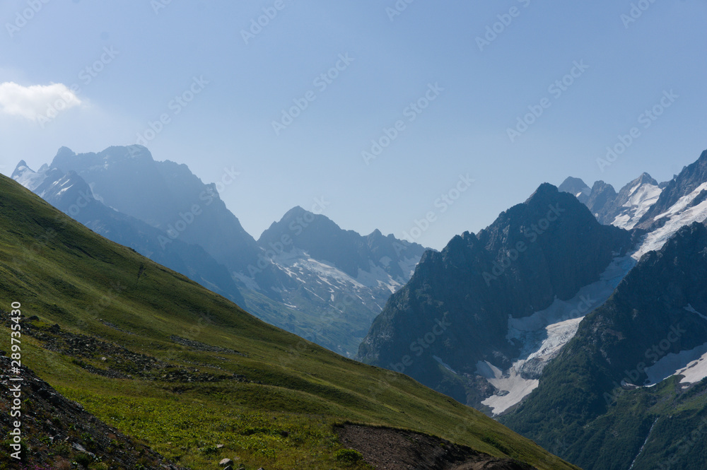 Fototapeta premium Mountain peaks in black, covered with glaciers and snow. green lush lawn meadows, Dombay, Russia, August 2019, raw original