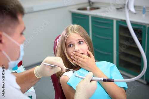 Frightened girl at the dentist s appointment. She closed her mouth in fear. She looks at the doctor  a fright in her eyes. Concept of prevention and treatment of teeth.