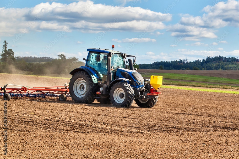 Obraz premium A blue tractor sows grain. Farm work on a farm in the Czech Republic. Tractor on a wheat field. Agricultural machinery.