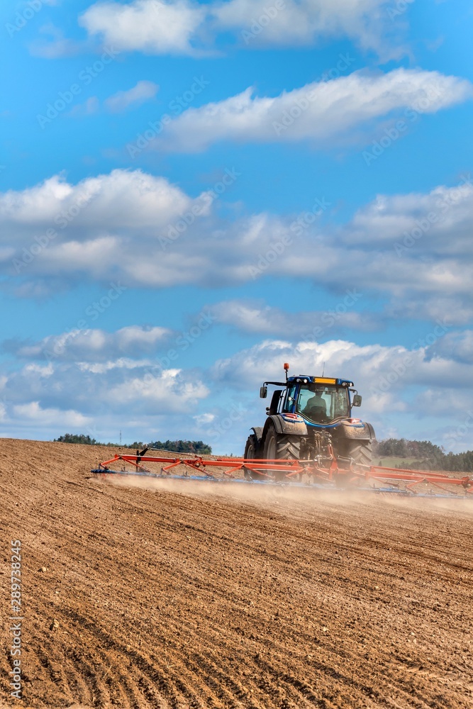 Fototapeta premium A blue tractor sows grain. Farm work on a farm in the Czech Republic. Tractor on a wheat field. Agricultural machinery.