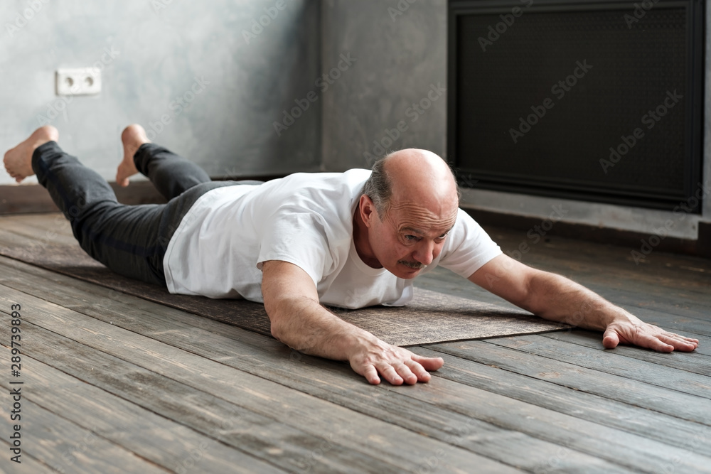 Senior hispanic man doing the Shalabhasana variation on exercise mat. Senior hispanic man doing the Shalabhasana variation on exercise mat.