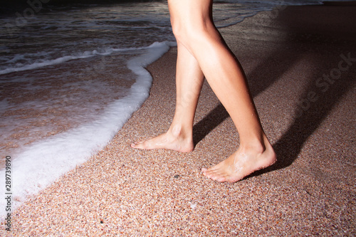 Close-up of female legs at the beach in the evening. Girl walking on the beach at night.