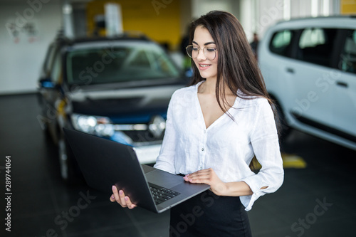 Saleswoman with laptop near new car in salon
