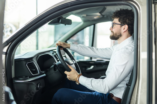 Handsome bearded man is sitting in a new car in car dealership